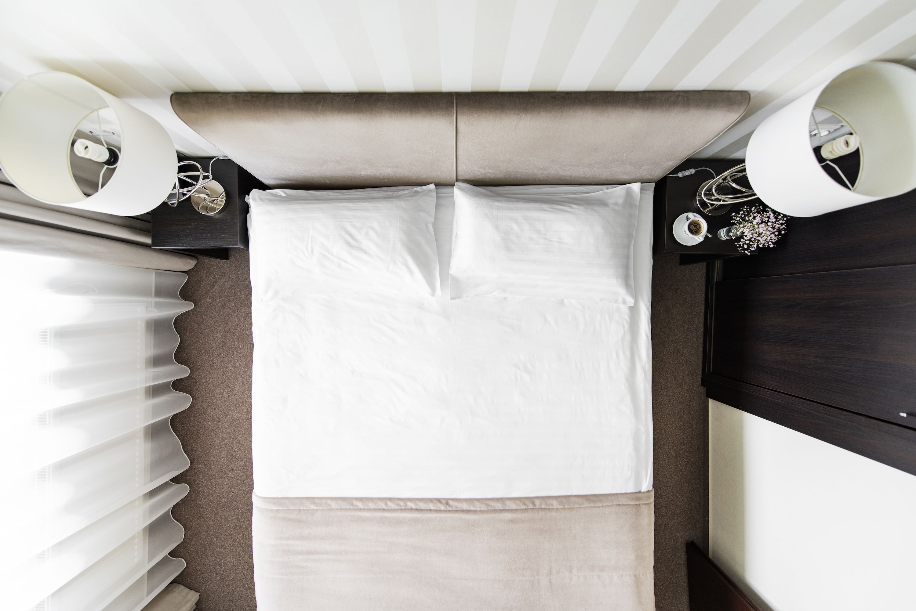 A neatly made bed with white linens, a dark headboard, and a bedside table with a lamp and a cup.