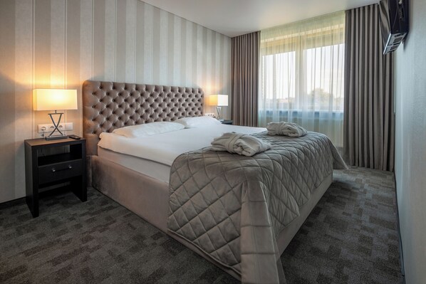 Habitación de hotel con una cama grande, una mesita de noche, una lámpara y vistas al exterior.