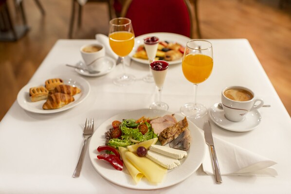 Desayuno servido con platos de comida, vasos de jugo de naranja y una taza de café sobre una mesa blanca.