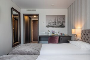 Habitación de hotel con cama, escritorio, silla, espejo, un cuadro y lámpara.