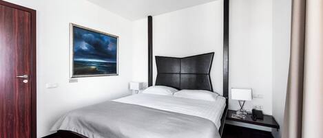 A hotel room with a bed, a nightstand, a lamp, a painting, and a door.