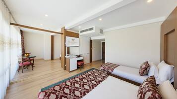 A hotel room with a bed, a desk, a chair, and a small table with a fruit bowl.