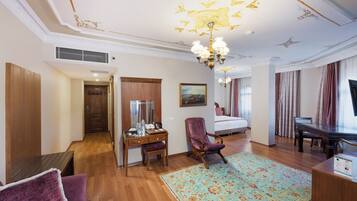 A hotel room with a wooden floor, a desk with a chair, a bed, a television, and a chandelier.