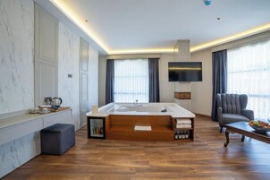 A modern bathroom with a large bathtub, a flat-screen TV, and a seating area with a table and chair.