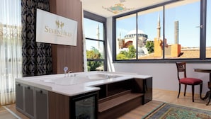 A modern bathroom with a large bathtub, a sink, and a glass-enclosed shower. There is a view of a mosque through the window. - Seven Hills Hotel - Special Class (Istanbul)