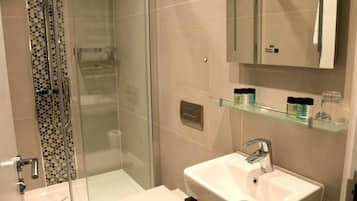 Un baño moderno con cabina de ducha de vidrio, un lavabo blanco y una repisa de vidrio con artículos de aseo.