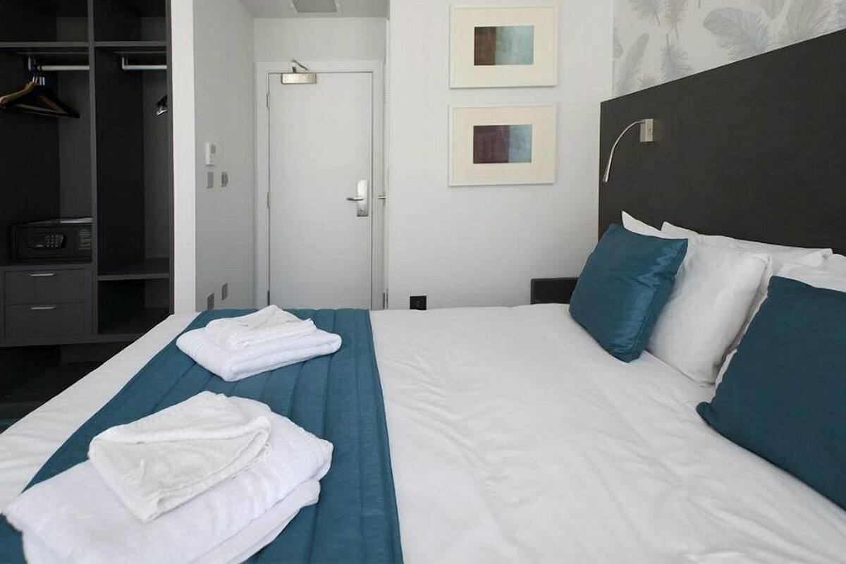 A hotel room with a neatly made bed, a wardrobe, and two framed pictures on the wall.