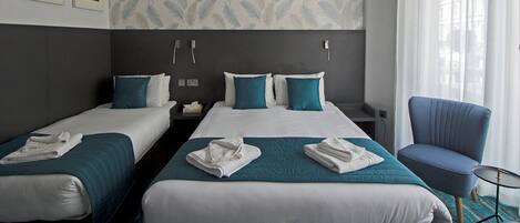 A hotel room with two beds, each with a teal bedspread and white linens, a blue armchair, and a small round table.