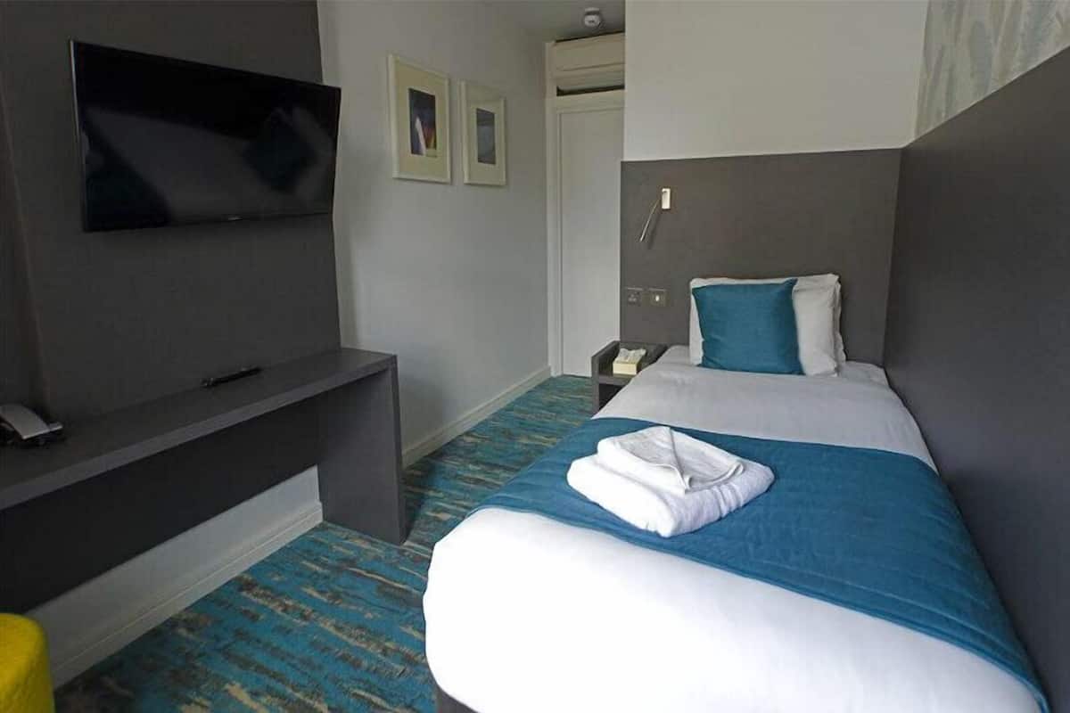 A hotel room with a bed, a TV mounted on the wall, a desk, and a door.