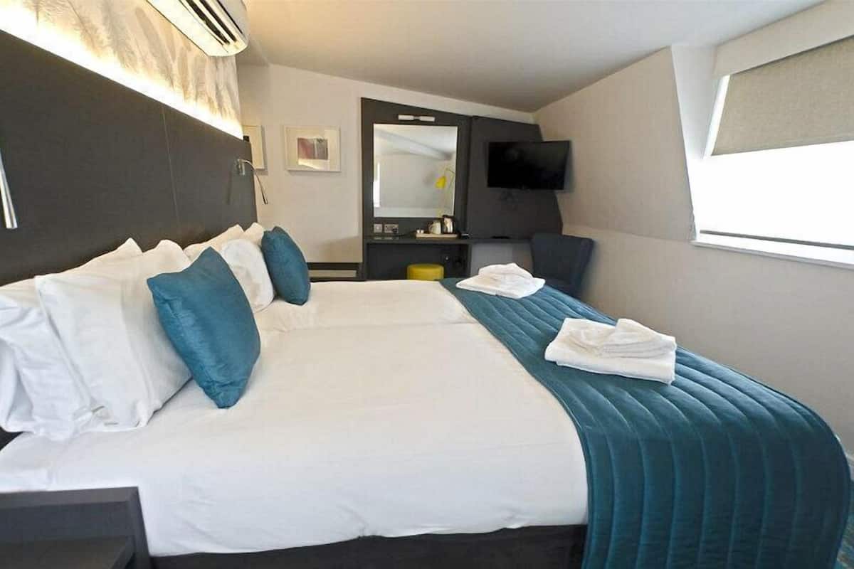 A hotel room with a large bed, a desk, a chair, a flat-screen TV, and a window with blinds.