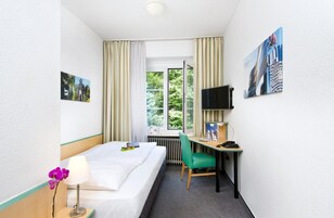 Una camera d'albergo con un letto, una scrivania, una sedia, una TV e una finestra con tende.