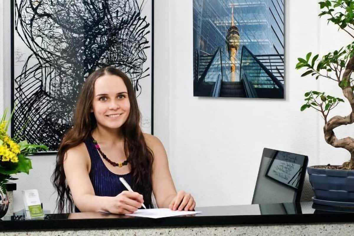 A reception desk with a framed abstract artwork, a bonsai tree, and a cityscape photo.