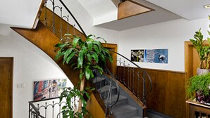 A staircase with a wooden handrail, carpeted steps, and a potted plant at the base.