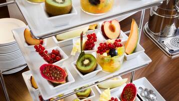 Ein mehrstöckiges Serviertablett mit verschiedenen Früchten und Desserts, darunter Kiwi, Melone und Beeren, auf einer Holztischplatte.