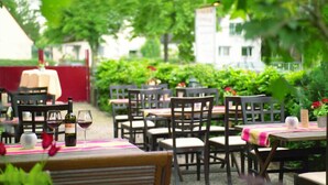 An outdoor dining area with tables and chairs, surrounded by greenery and a building in the background. - Hotel Zum Zeppelin (Hamburg)