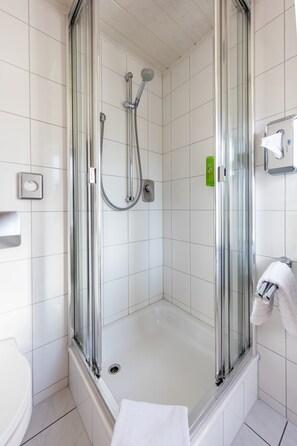 Shower area features a clear glass door and a wall-mounted showerhead with a control panel nearby.