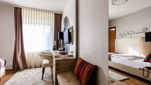 A modern hotel room with a sofa, a bedside table, a desk with a chair, a large bed, and a bathroom with a mirror and sink. - Hotel Zum Zeppelin (Hamburg)
