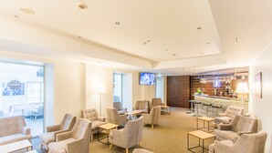 Un hall d’hôtel doté de plusieurs espaces salon, d’un téléviseur et d’un bar.