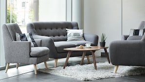Un salon moderne avec un canapé gris, deux fauteuils, une table basse et une lampe.
