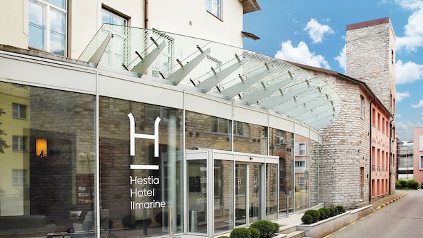 Un hôtel moderne doté d’une façade en verre, d’un logo en forme de « H » bien visible et d’une façade en pierre sur l’un de ses côtés.