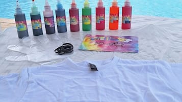 Montagem à beira da piscina com tecido branco, guia passo a passo de um projeto e garrafas coloridas com tie-dye.