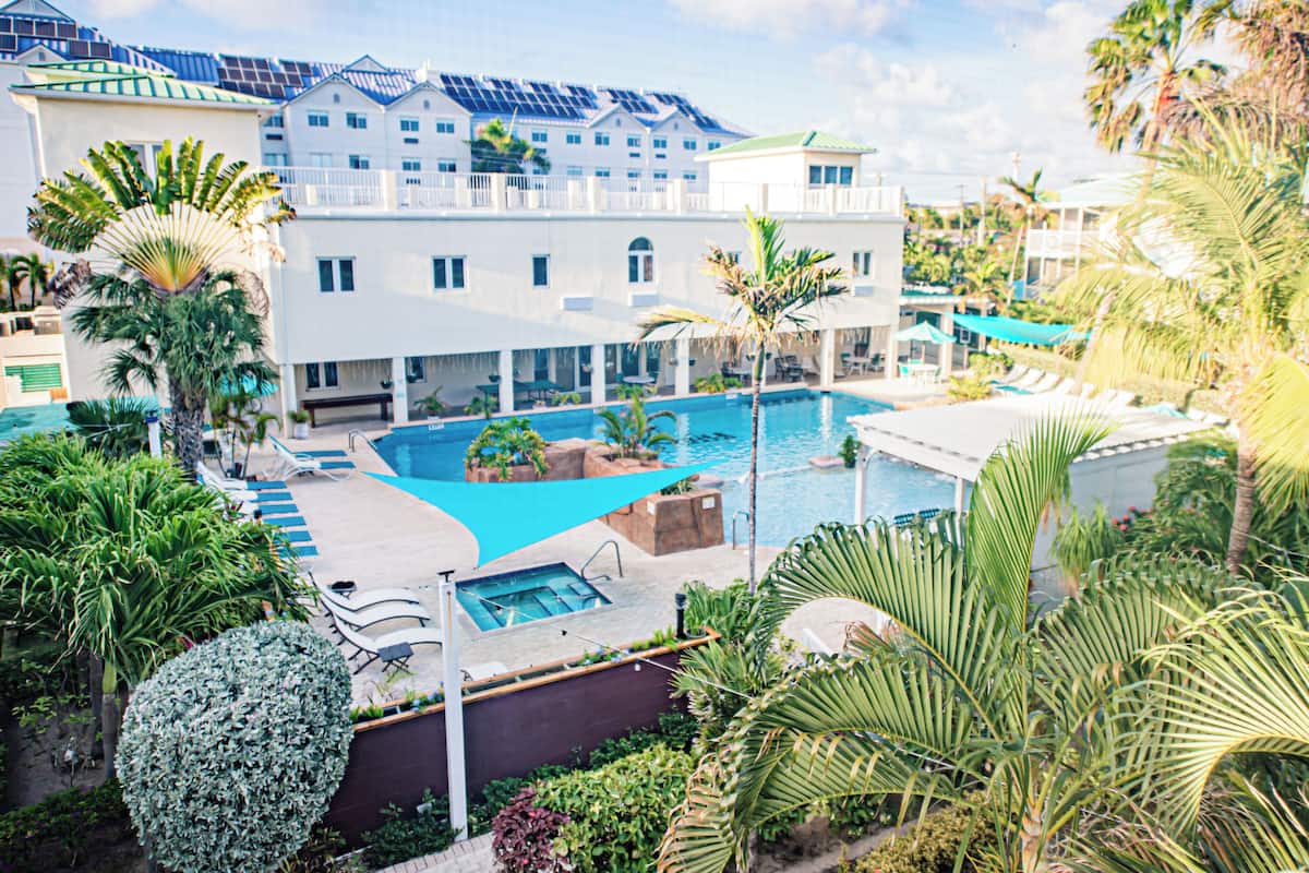 A hotel with a large swimming pool, multiple lounge areas, and lush tropical landscaping.