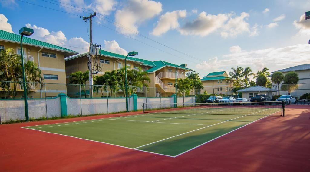 A tennis court with a net, surrounded by buildings with green roofs and a clear sky.