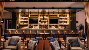 Eine Barbereich mit verschiedenen Sitzmöglichkeiten, darunter Barhocker und runde Tische, mit einer gut sortierten Bar im Hintergrund.
