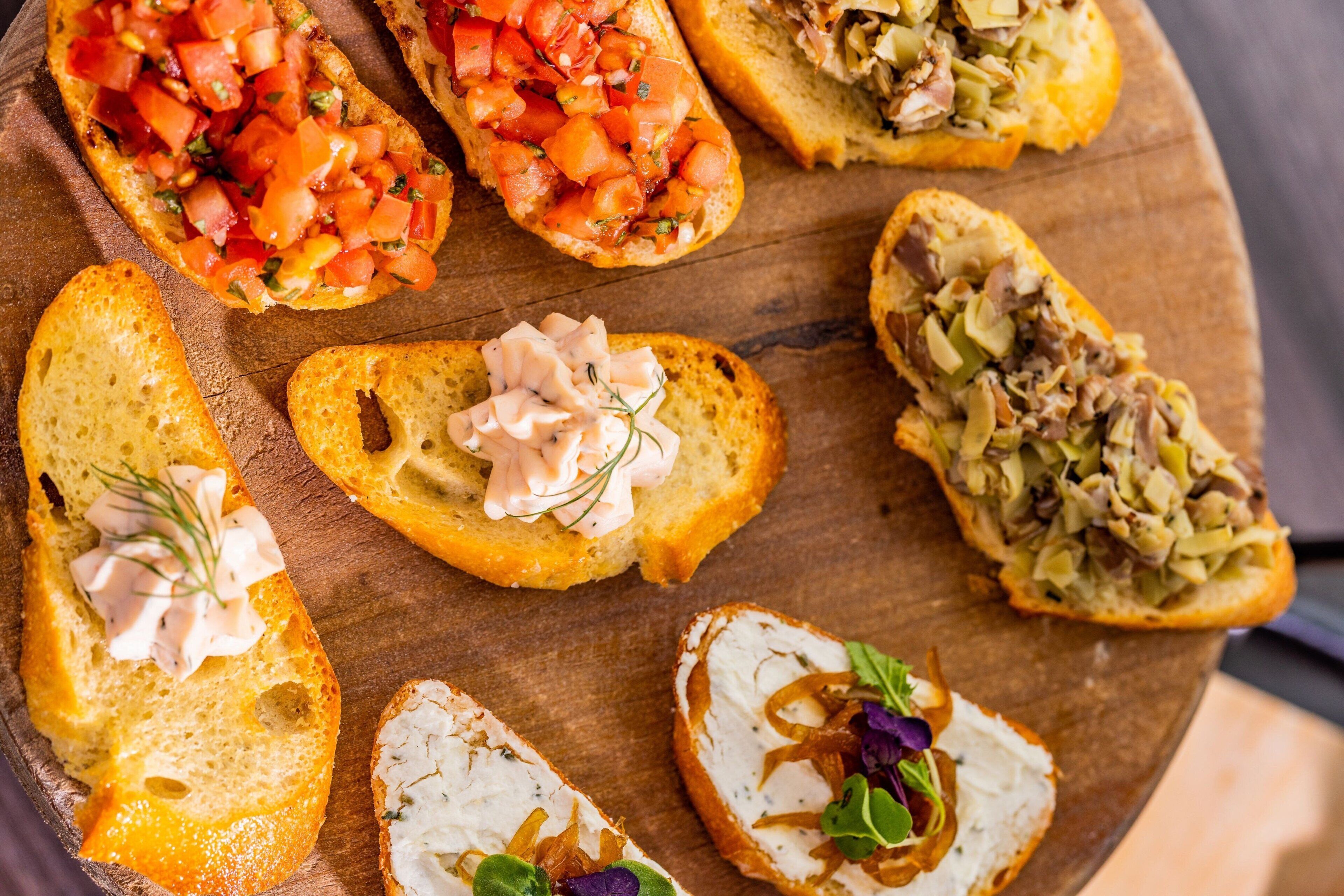 A wooden board with various bruschetta toppings.