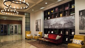 Eine Lobby mit einem roten Sofa, gelben Ohrensesseln, einem gemusterten Teppich und einer Wand mit verschiedenen Dekorationselementen.