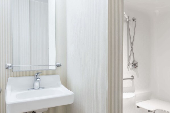 Un baño con lavamanos blanco, un espejo y zona de ducha.