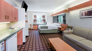 Une chambre d’hôtel compacte comprenant un coin cuisine, un lit avec une couvre-lit verte, un canapé, une table de chevet et une fenêtre avec des rideaux.