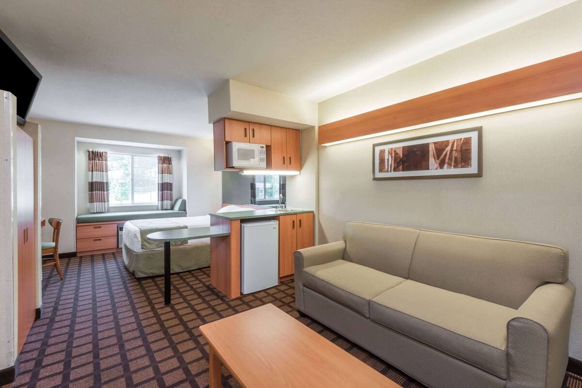 A compact room with a kitchenette, a sofa, a small table, and a window with curtains.