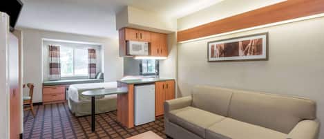 A compact room with a kitchenette, a sofa, a small table, and a window with curtains.