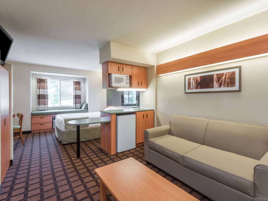 A compact room with a kitchenette, a sofa, a small table, and a window with curtains.