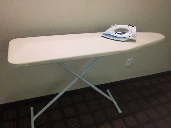 A white ironing board with a blue and white iron on top, positioned against a wall with a patterned floor. - Microtel Inn & Suites by Wyndham Uncasville Casino Area (Montville)