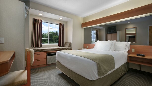 Une chambre d’hôtel avec un grand lit, un bureau, une chaise, une fenêtre avec des rideaux et un téléviseur.
