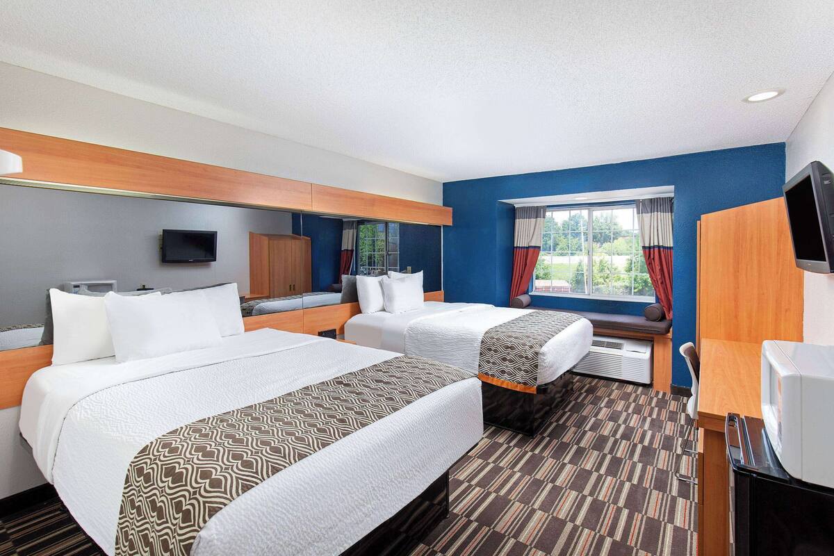 A hotel room with two beds, a television, a desk, and a window with curtains.