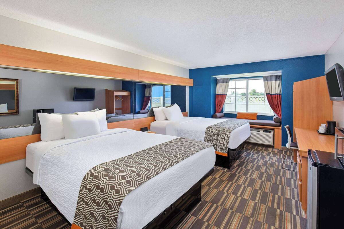 A hotel room with two beds, a desk, a chair, a TV, and a window with curtains.