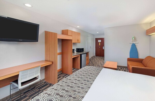 Una habitación de hotel compacta con televisión de pantalla plana, kitchenette, sofá y cama.