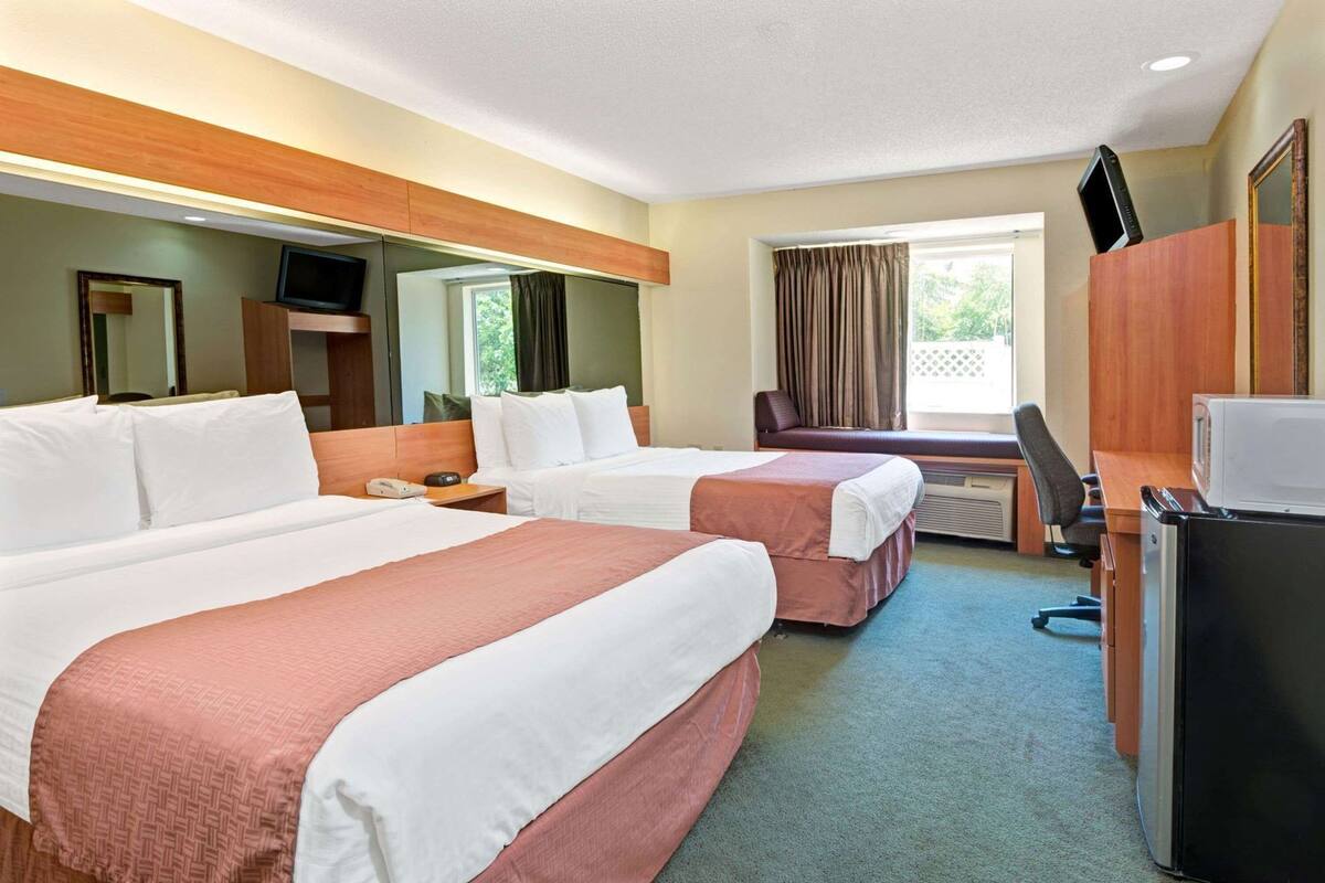A hotel room with two beds, a desk, a television, and a microwave.