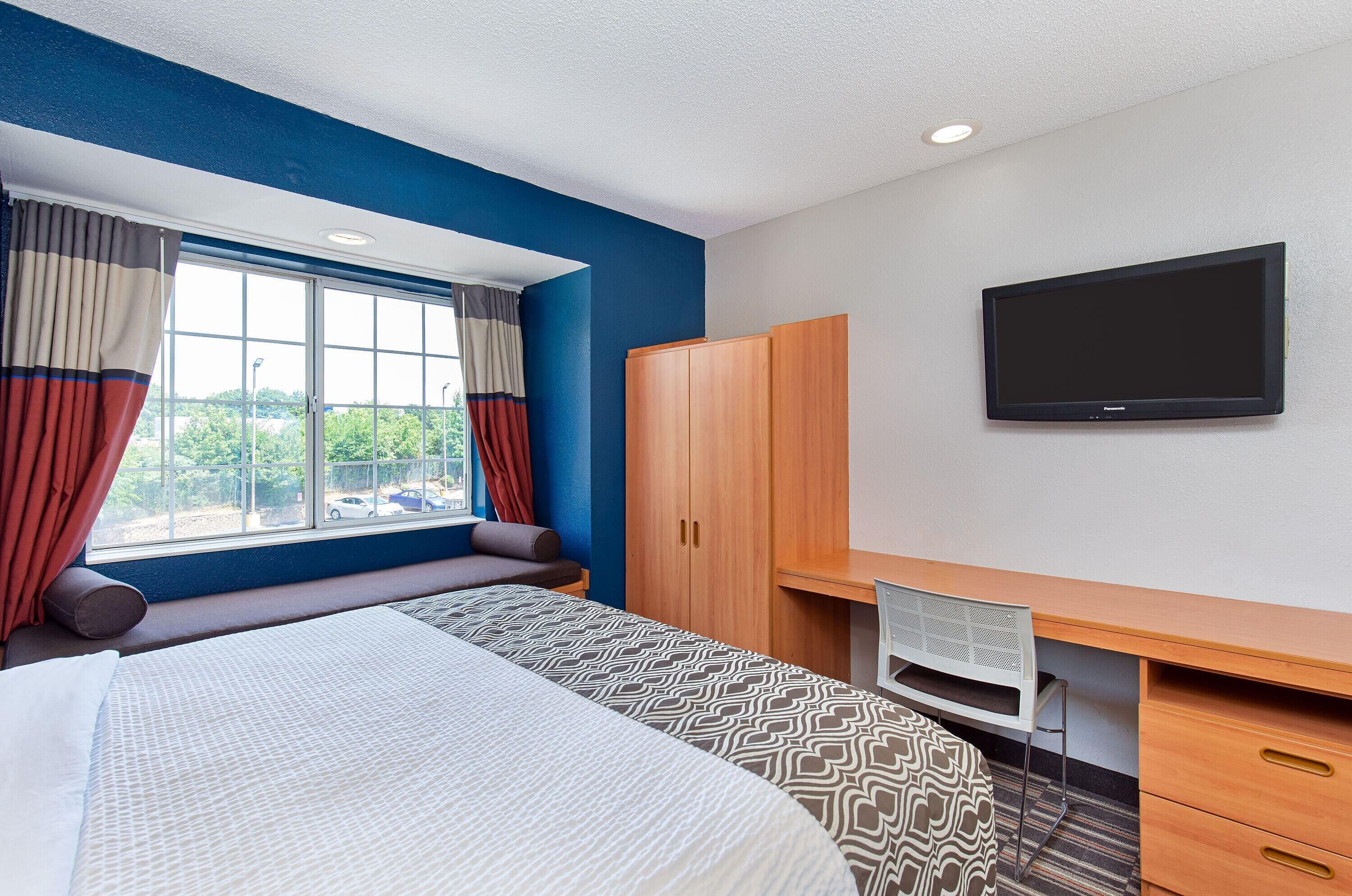 Une chambre d’hôtel avec un lit, un bureau, une télévision et une fenêtre avec des rideaux.