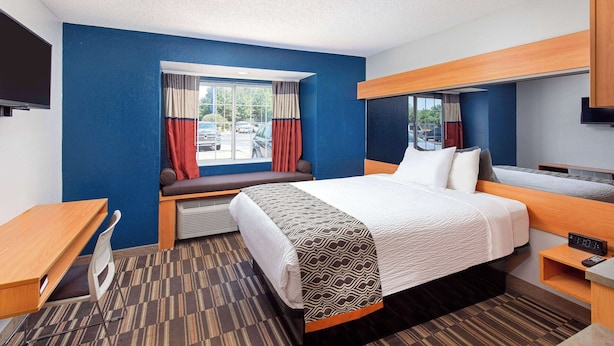 Een hotelkamer met een bed, bureau, stoel, televisie en raam met gordijnen.