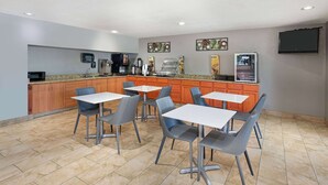 Een moderne keuken met een koffiehoek, een koelkast en een magnetron. Er staan meerdere tafels en stoelen klaar voor diners.