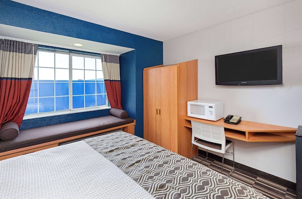 Una habitación de hotel con cama, escritorio con microondas, televisor y ventana con cortinas.