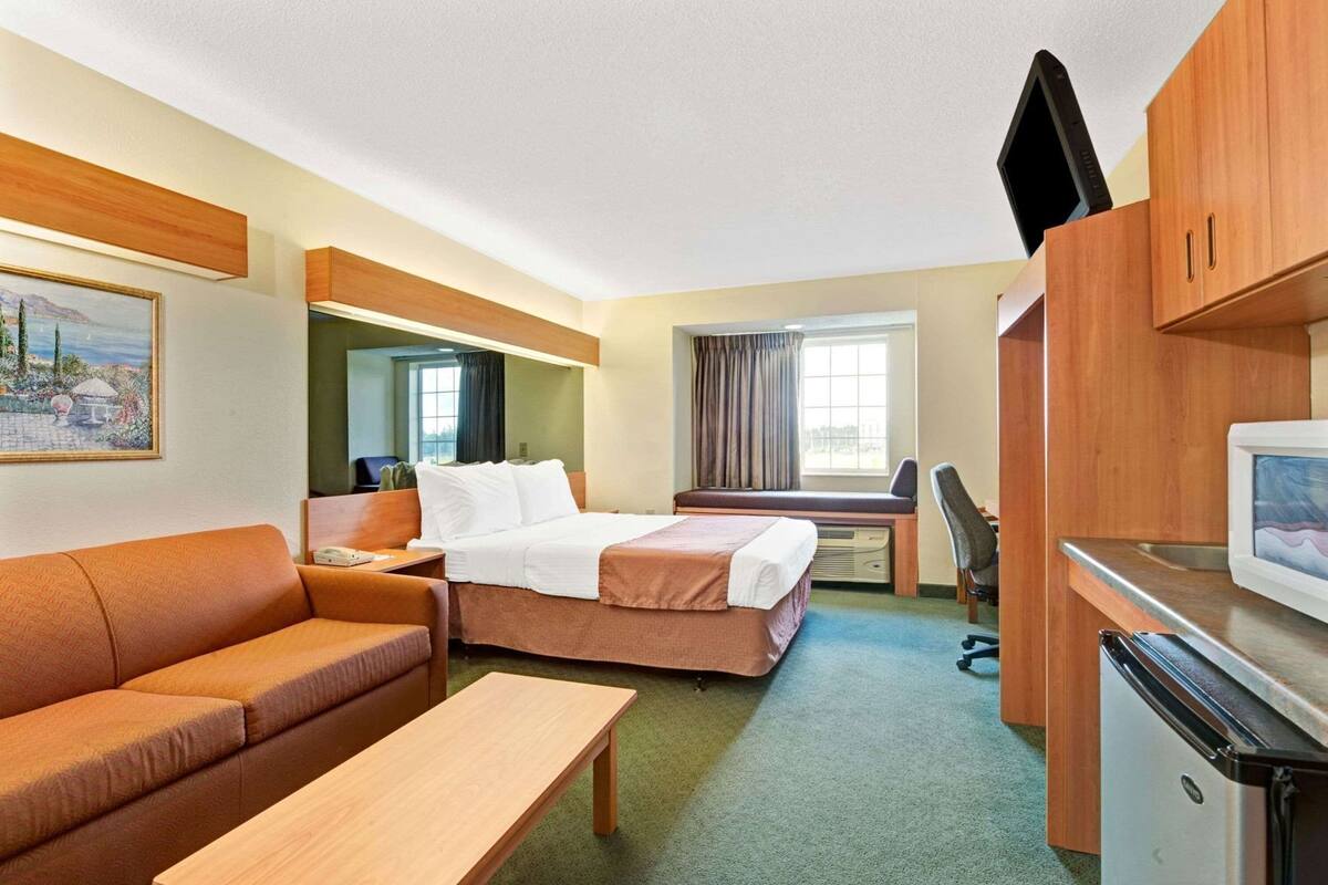A hotel room with a bed, a sofa, a desk, a chair, a television, and a refrigerator.