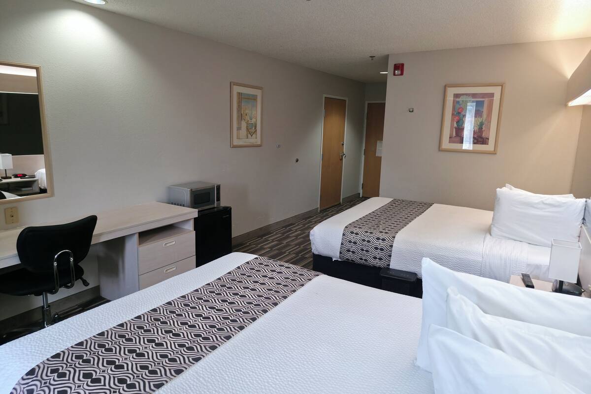 A hotel room with two beds, a desk, a chair, a microwave, and a small refrigerator.