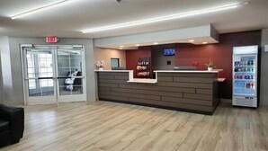 Una recepción con mostrador, pantalla digital, refrigerador con bebidas y puerta de cristal.