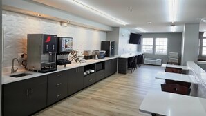 Una cocina moderna con cafetera integrada, microondas y refrigerador. Hay taburetes de bar y una zona de comedor con una encimera larga.