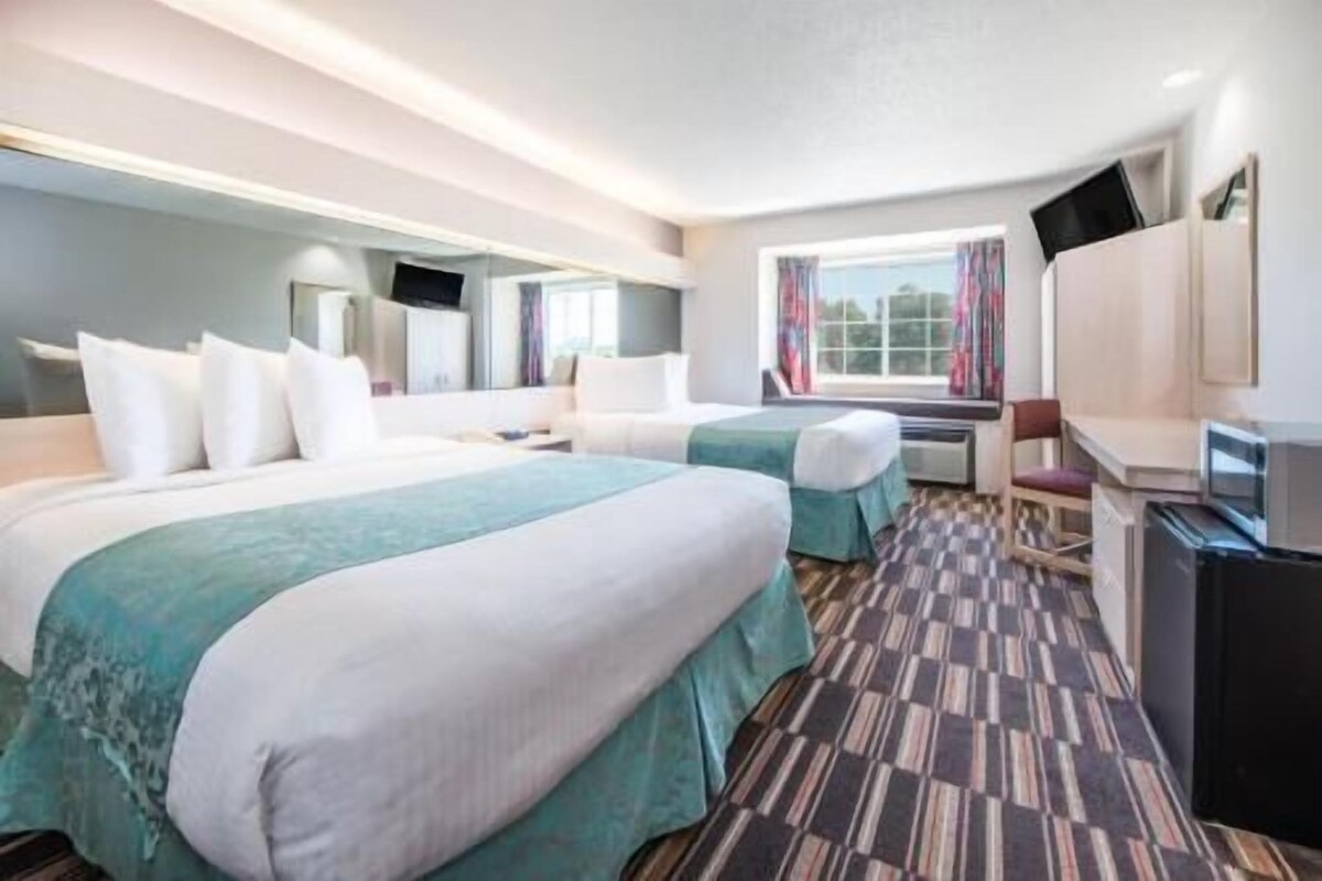 A hotel room with two beds, a desk, a chair, a television, and a window with curtains.